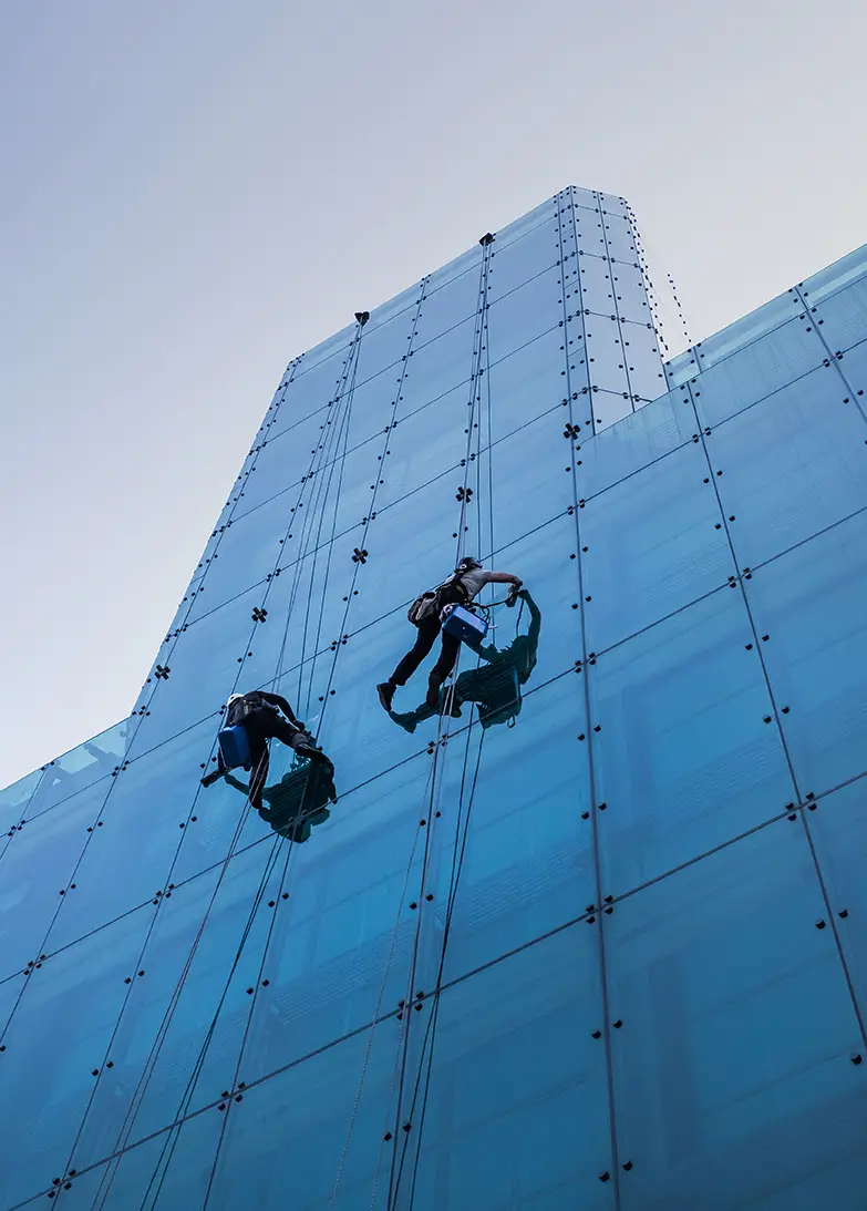 vertical-low-angle-shot-two-people-climbing-tall-glass-building-day-time copy